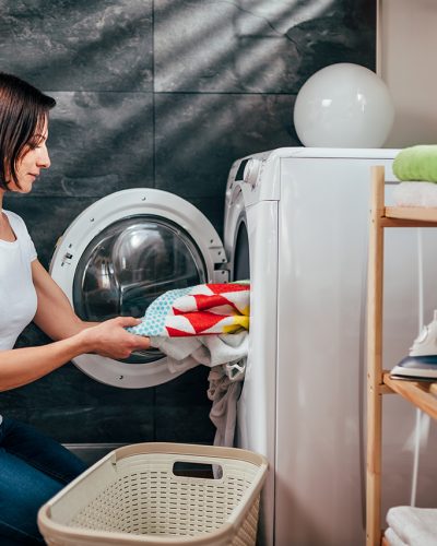 Woman wearing white shirt taking clothes out washing machine at laundry room